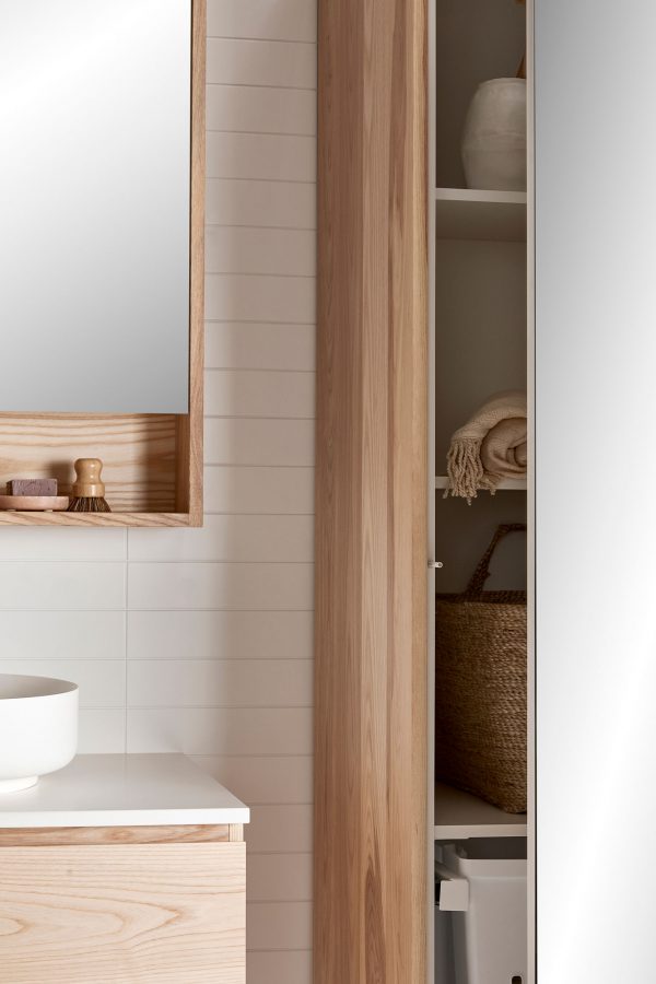 A tall timber storage unit with the door open in a coastal bathroom setting