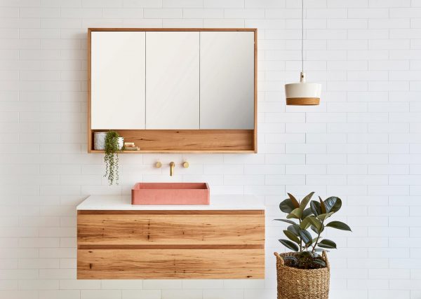 Mirrored bathroom cabinet with a storage shelf above a single sink floating timber vanity. The timber vanity has a pink stone sink.