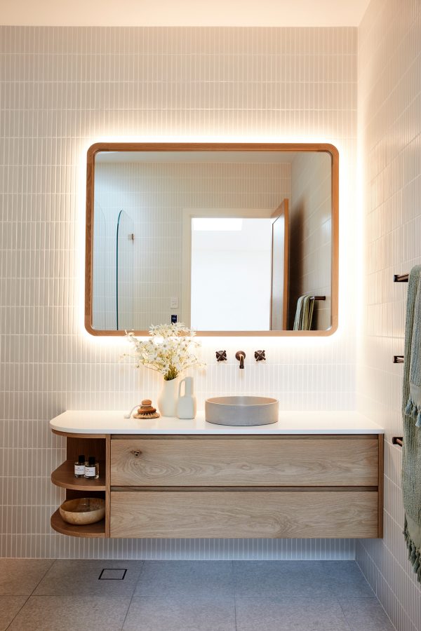 A contemporary bathroom featuring a curved timber wall hun vanity under a custom design timber mirror.