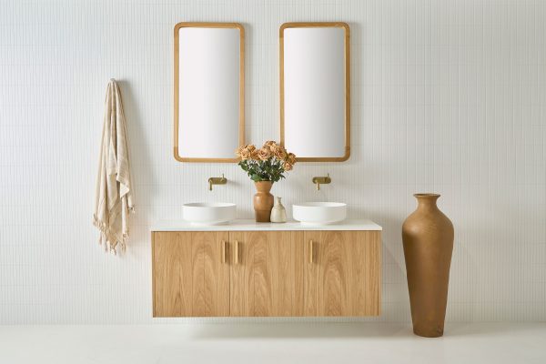 Modern bathroom furniture. This 3 door wall hung solid timber vanity is sat underneath 2 rectangular mirrors. A white stone bench top sits atop this timber vanity with 2 white sinks with gold tapware | Loughlin Furniture
