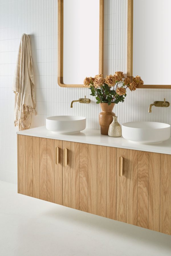 A 3 door Wall hung solid timber vanity inside an Australian coastal bathroom. A White Stone bench top with white sinks and gold tapware sits below two rectangular mirrors | Loughlin Furniture
