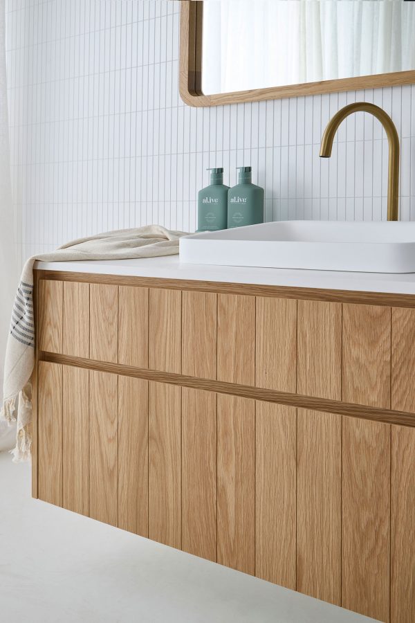 Australian coastal bathroom setting with two drawer custom made timber vanity. Wall hung this has two drawers. It has a white sink and gold tapware.
