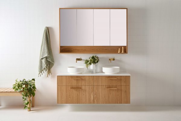 A four drawer custom made timber vanity. Set in this coastal bathroom is this wall hung vanity with a white bench top and two sinks. It sits underneath a custom made wooden vanity mirror.