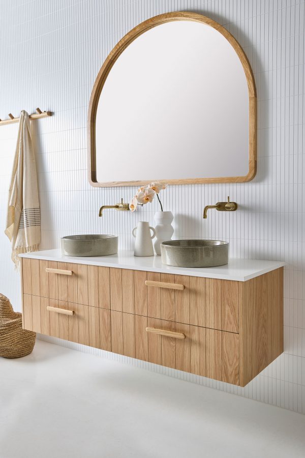 A four drawer timber vanity with coastal bathroom furniture. This wall hung timber and stone vanity with stone sinks sits against white finger tiles under an Alura arch mirror.