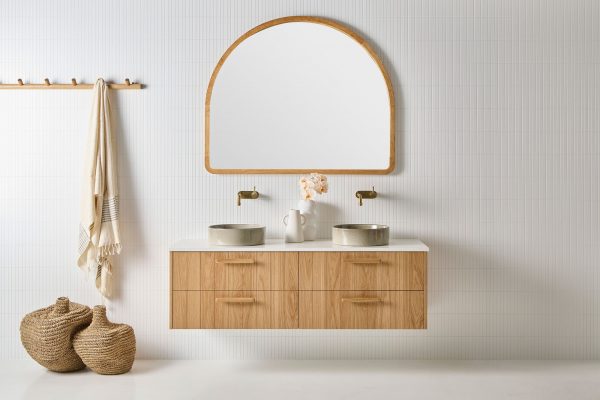 A coastal bathroom with four drawer timber vanity. This wall hung timber and stone vanity sits against white finger tiles with an alura arch mirror.