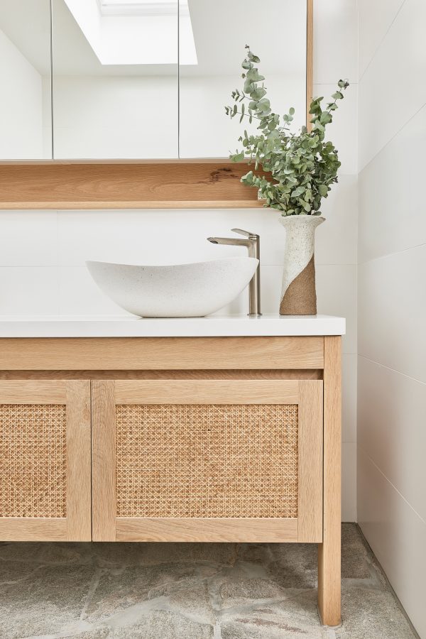 A coastal bathroom that features a freestanding rattan door vanity with white basin and sliver tap ware