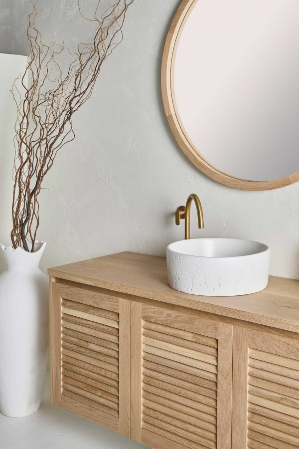 A Loughlin Furniture real timber vanity with a stone basin and gold tapwear. The wall mounted vanity with timber louvre door profile sits under a custom round mirror from the Alora range.