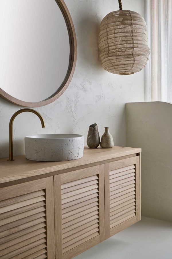 This Loughlin Furniture wall mounted timber vanity sits in a modern coastal bathroom with a stone sink and brass tapware. It sits below the Alura Round custom made mirror.
