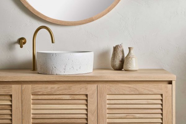 This Loughlin Furniture wall mounted timber vanity sits in a modern coastal bathroom with a stone sink and brass tapware. It features Louvre Panel Profile.