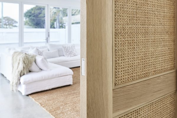Internal cavity custom made sliding door with open weave rattan with a bright lounge room behind it. Custom made by Loughlin Furniture.