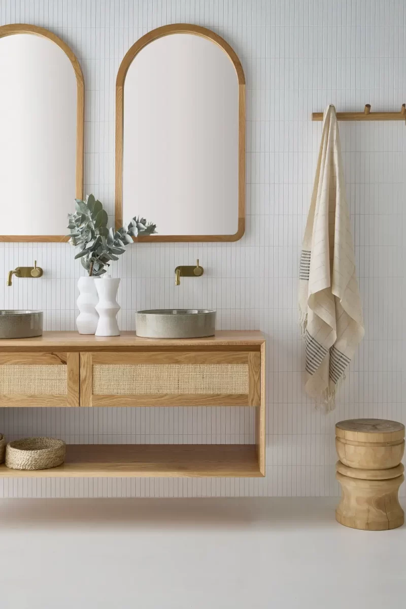 A twin wall hung vanity from the Loughlin Furniture Pacific Baxter Range. With open shelving and a single rattan profile drawer this is set in a costal bathroom under an Alura arch mirror