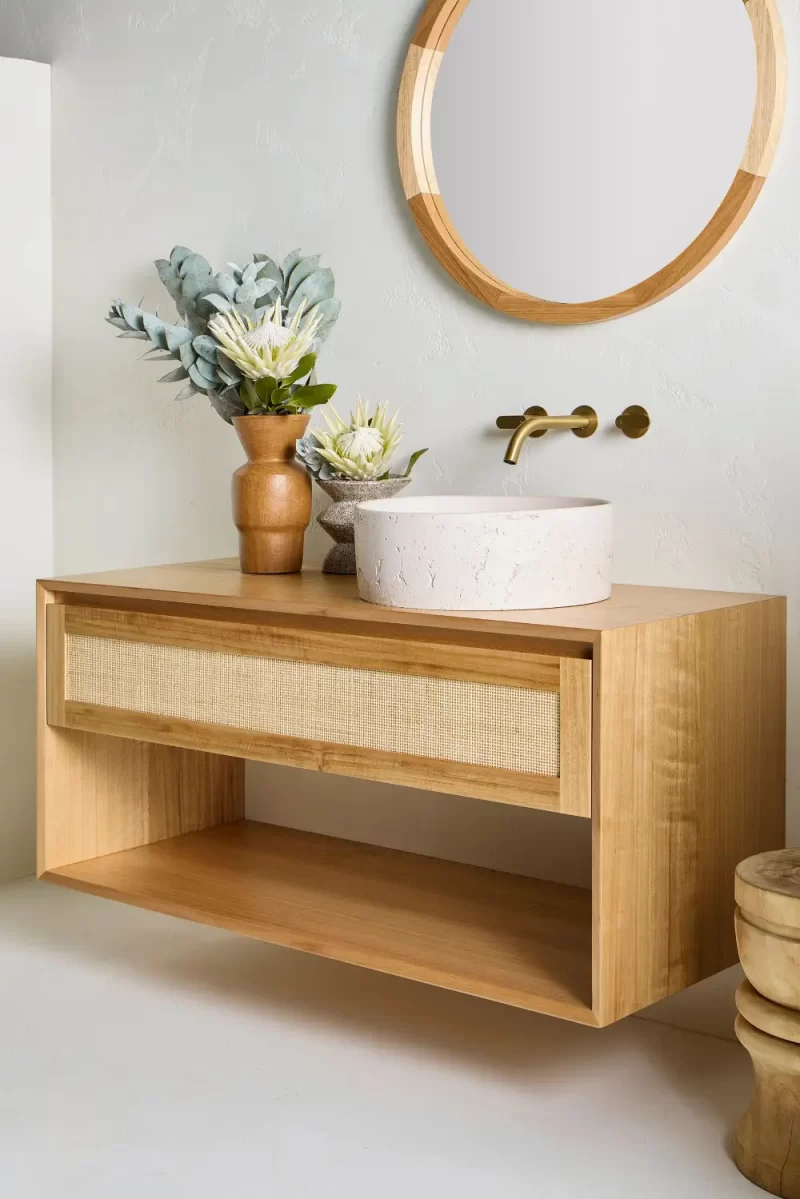 A single wall hung vanity from the Loughlin Furniture Pacific Baxter Range. With open shelving and a single rattan profile drawer this is set in a coastal bathroom under an Alura round mirror.