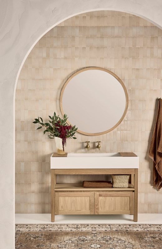 Timber bathroom vanity with open shelves and a double cupboard underneath a round mirror.